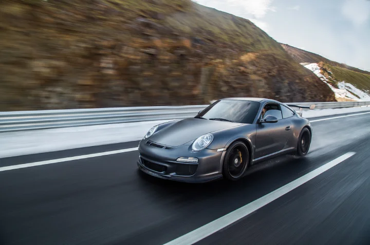 Matte grey sports car speeding on a scenic mountain highway during a premium car rental test drive.