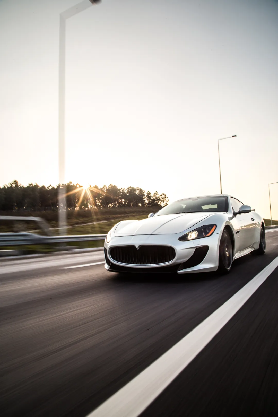 Silver luxury sports car driving forward under sunset light for premium vehicle rentals.